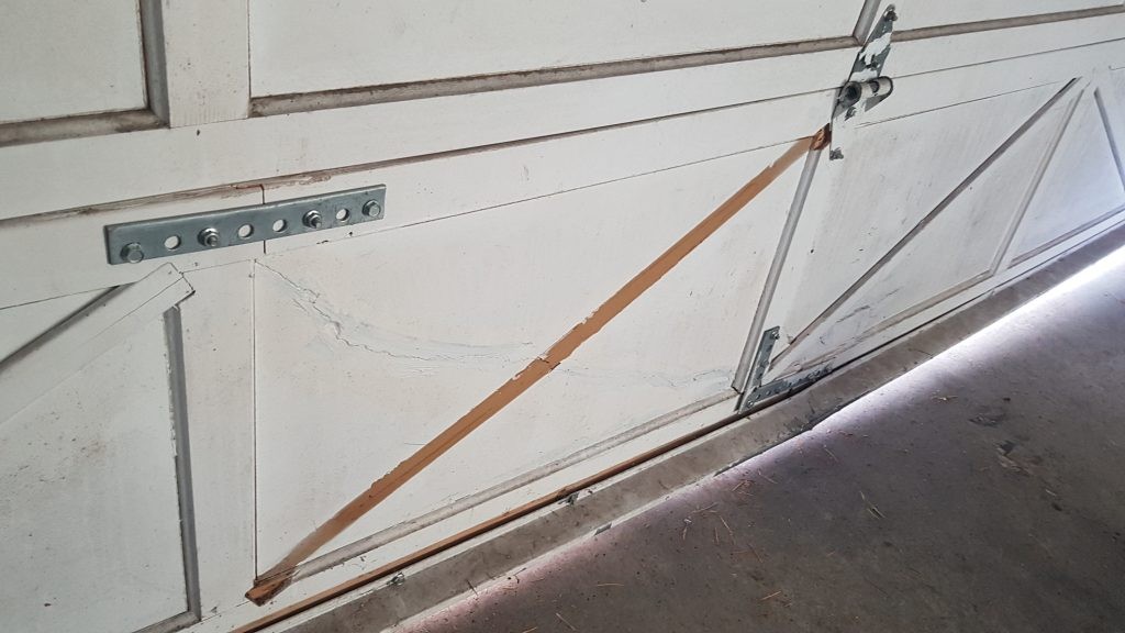 Bottom section of garage door that has a bent strutt and damaged panels.